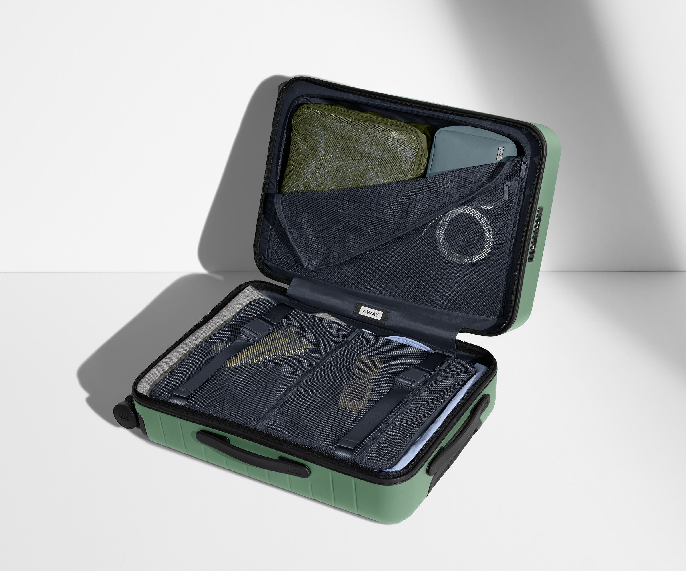 The Bigger Carry-On suitcase in Sea Green shown open on its side and packed with Away's packing organizers to show capacity and the interior compression system, designed to help you pack more in