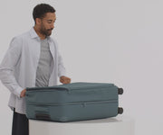 A male model filling The Softside Large suitcase in Coast Blue with Away's packing organizers and using the interior organization and compression system for seamless packing