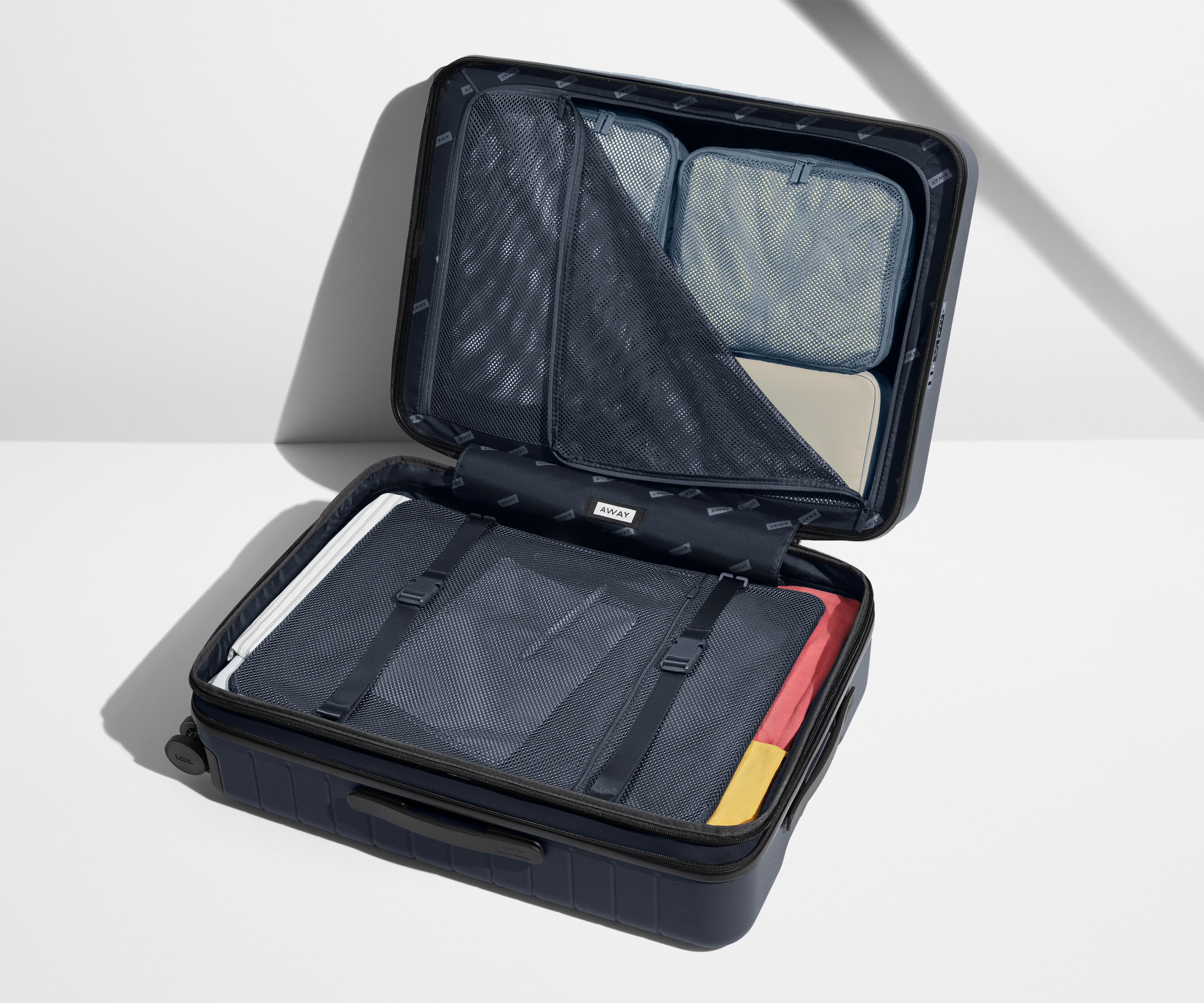 The Medium Flex suitcase in Navy Blue shown open on its side and packed with Away's packing organizers to show capacity and the interior compression system, designed to help you pack more in