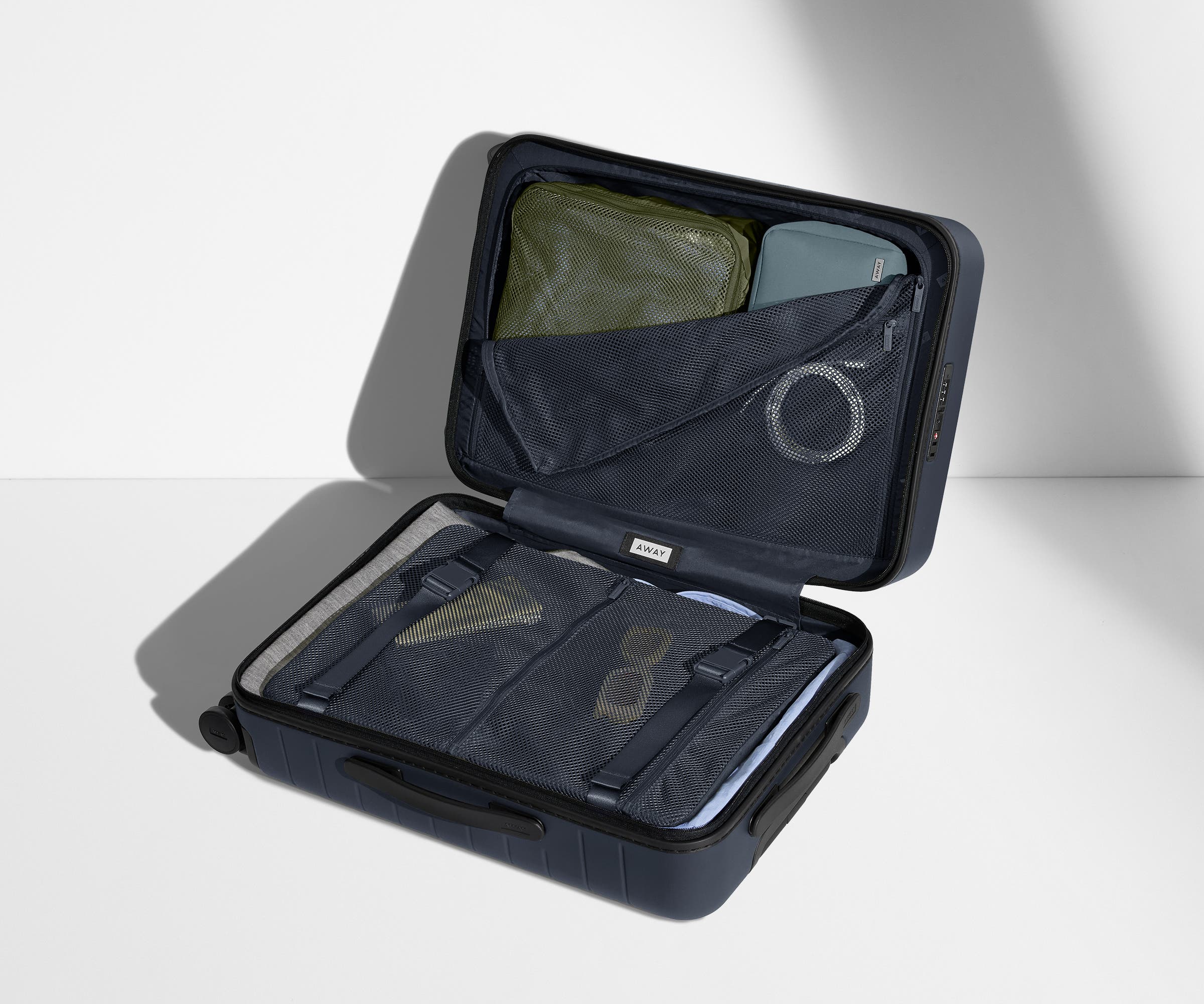 The Bigger Carry-On suitcase in Navy Blue shown open on its side and packed with Away's packing organizers to show capacity and the interior compression system, designed to help you pack more in