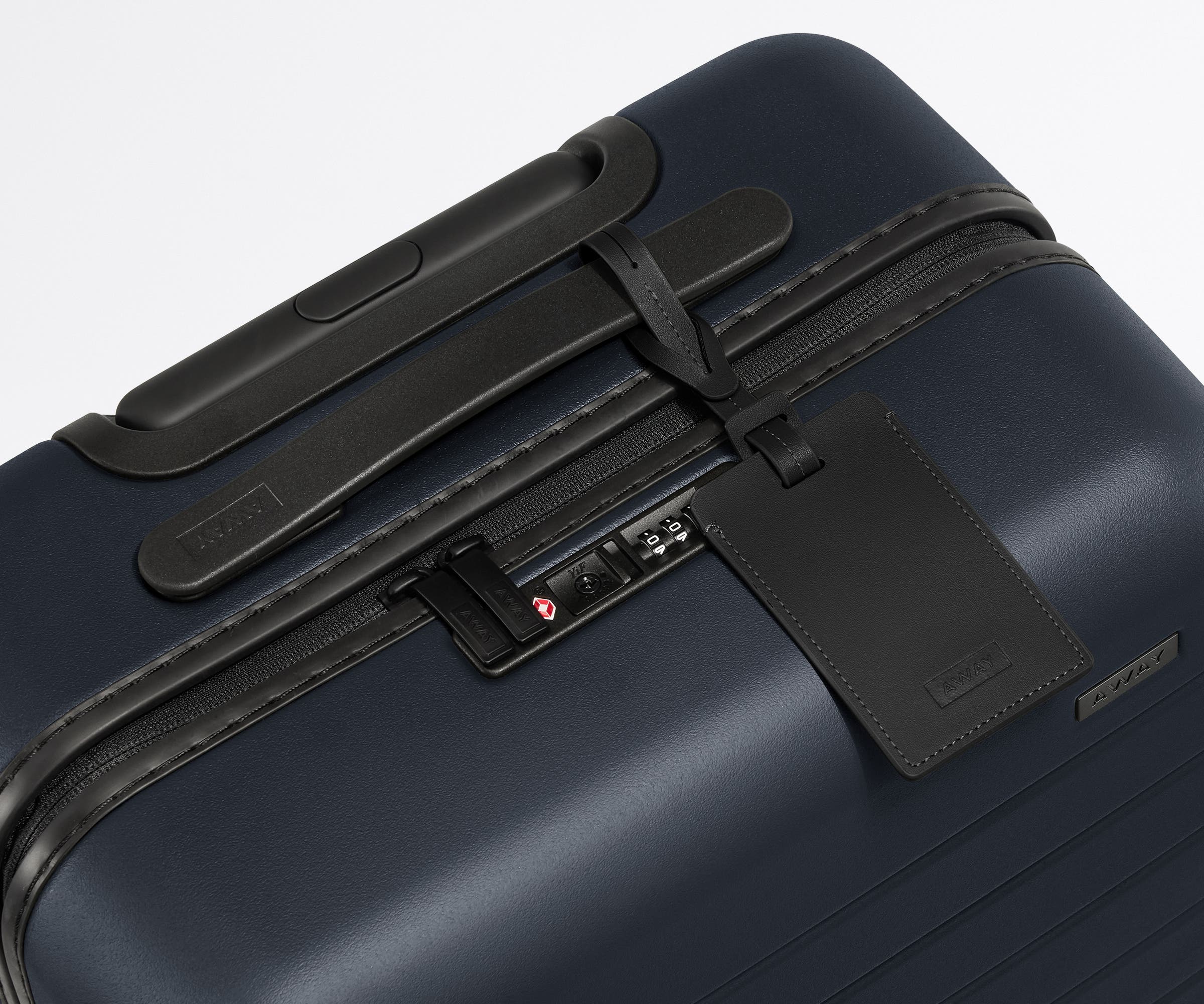 The Bigger Carry-On suitcase in Navy Blue shown shown from above highlighting TSA-approved combination lock and recycled leather luggage tag