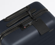 The Bigger Carry-On suitcase in Navy Blue shown shown from above highlighting TSA-approved combination lock and recycled leather luggage tag
