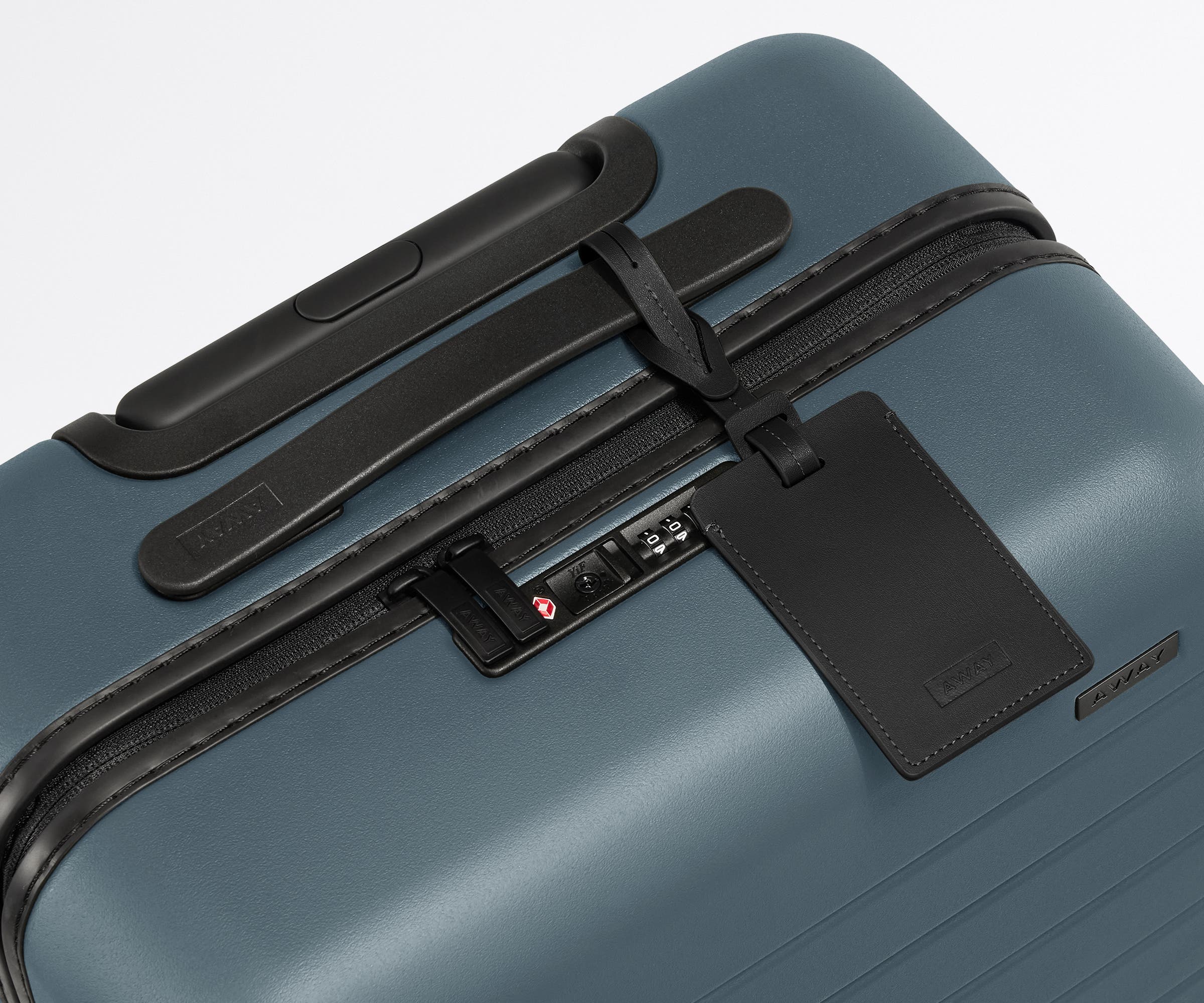 The Bigger Carry-On suitcase in Coast Blue shown shown from above highlighting TSA-approved combination lock and recycled leather luggage tag