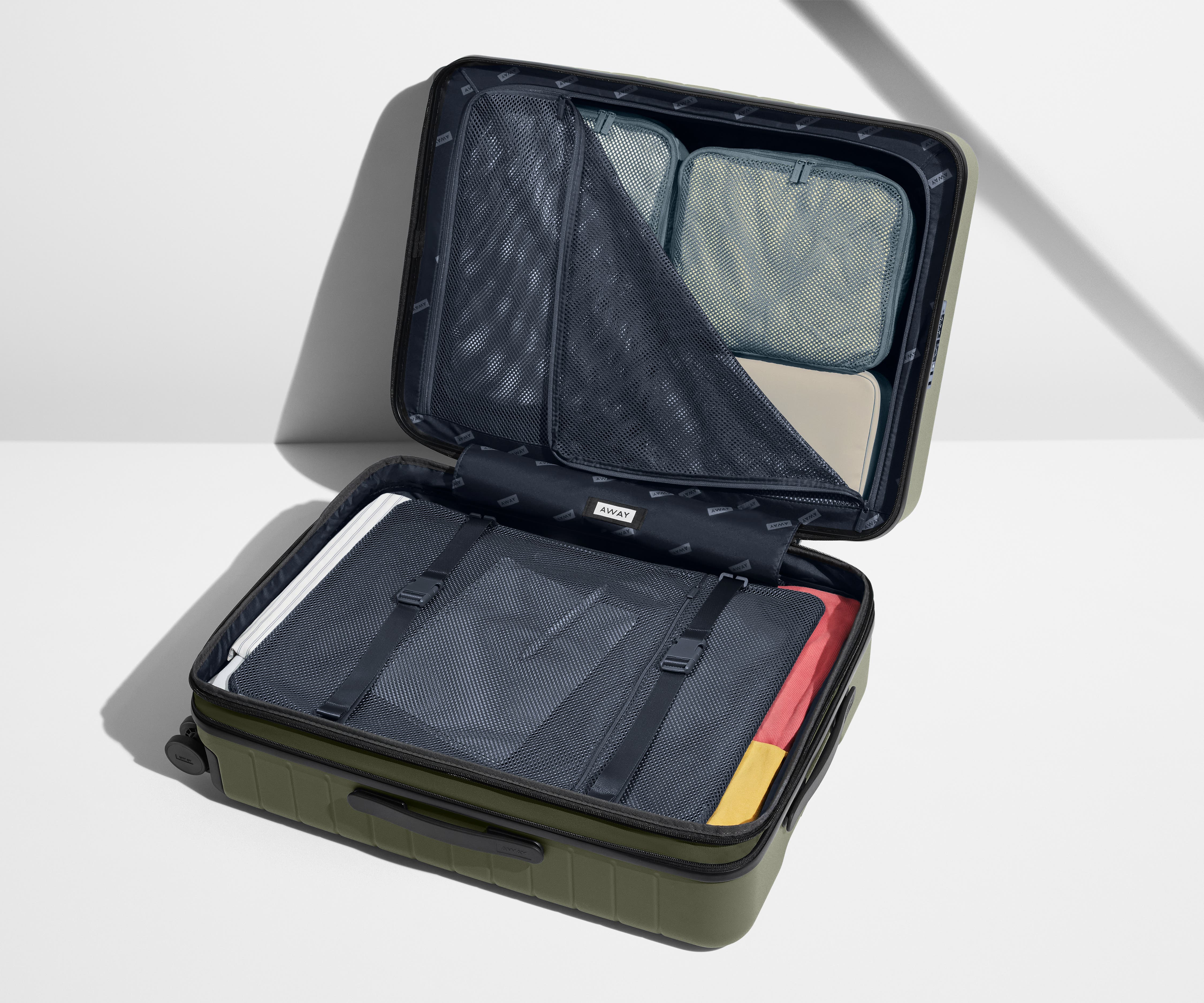 The Medium Flex suitcase in Sea Green shown open on its side and packed with Away's packing organizers to show capacity and the interior compression system, designed to help you pack more in