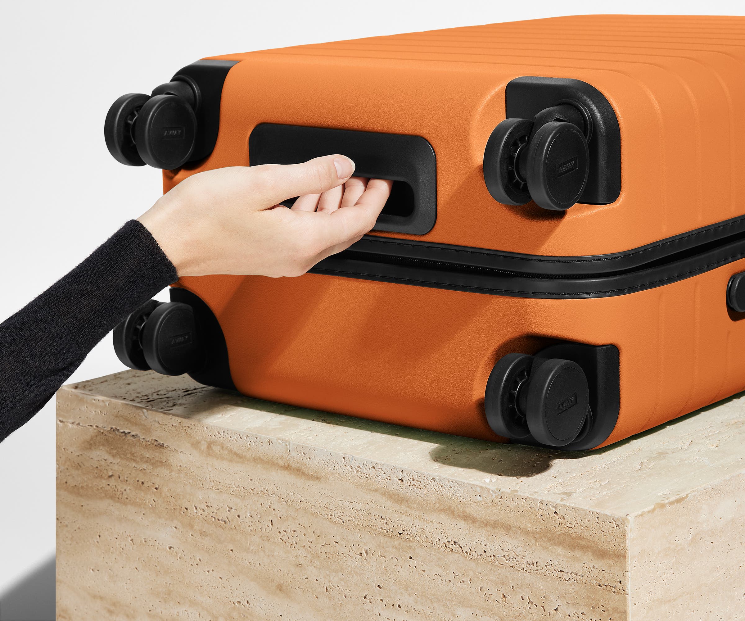 The Bigger Carry-On suitcase in Sorbet Orange shown from below highlighting the underside grab handle