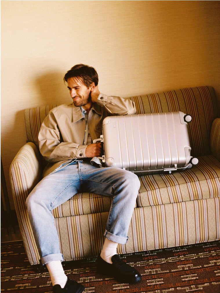 Male presenting person sitting on a couch with an Aluminum suitcase
