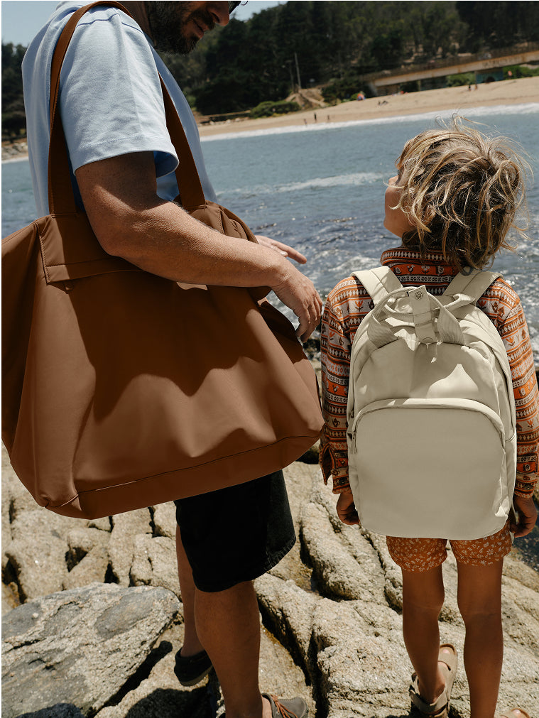 Parent wearing a Large Featherlight Tote and child with a Featherlight Backpack by the sea