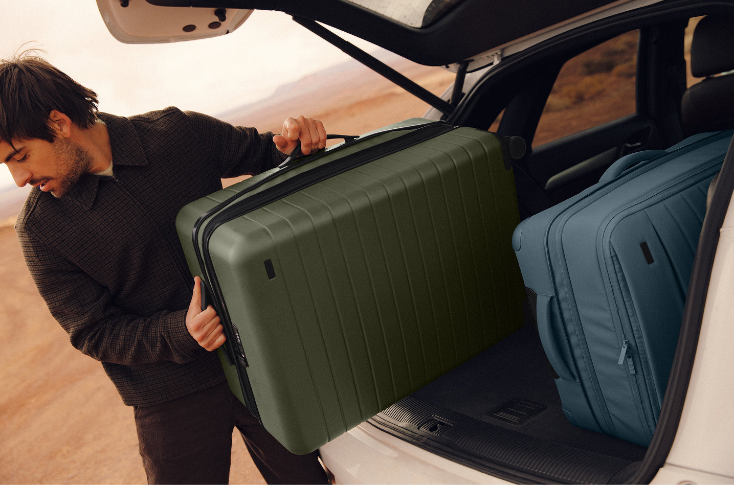 A person carrying an expandable Flex suitcase and Softside luggage from their trunk