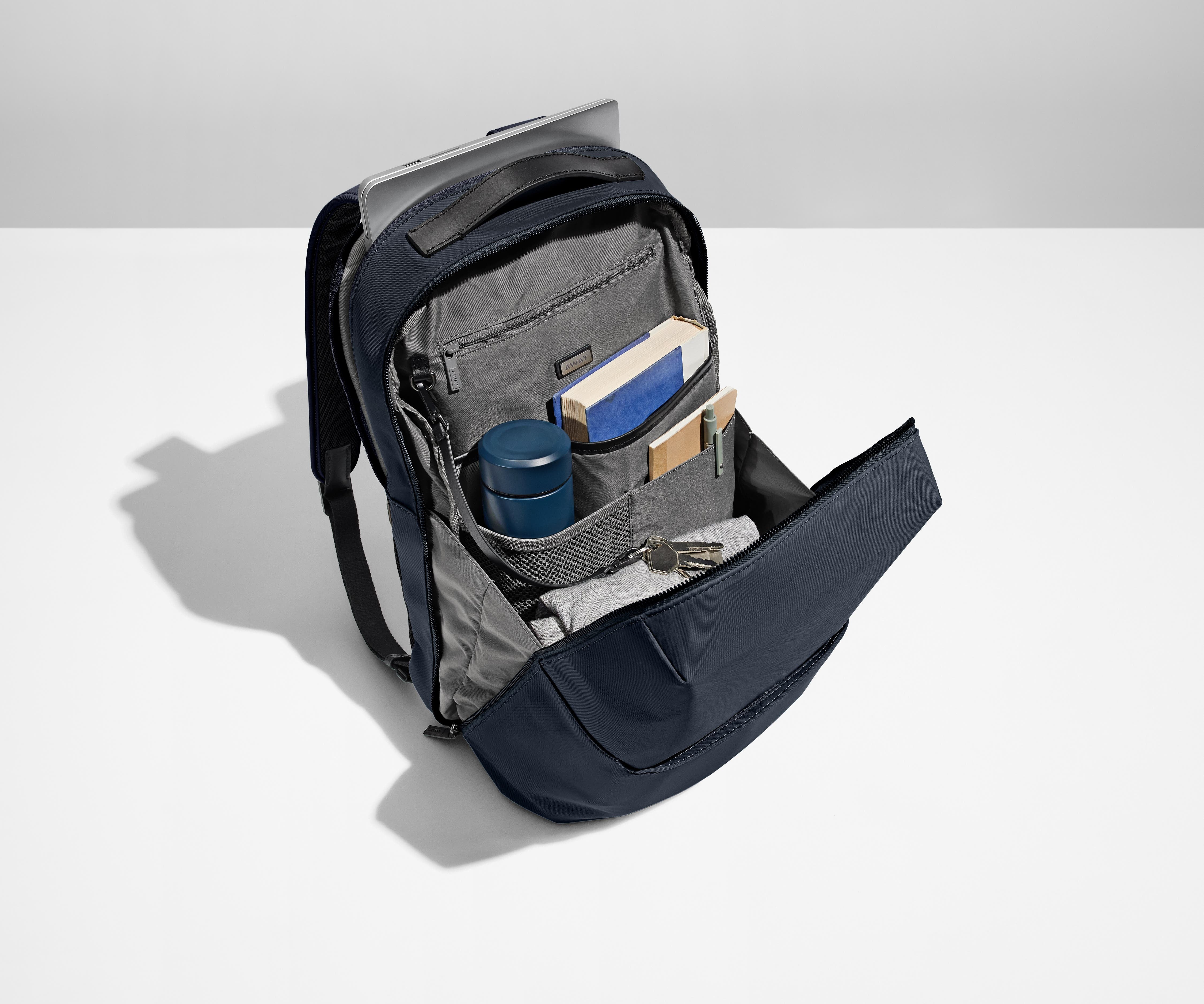 Everywhere Zip Backpack main compartment packed with a water bottle, books, clothing, and a key attached to the interior key leash. A laptop is packed in the exterior laptop pocket