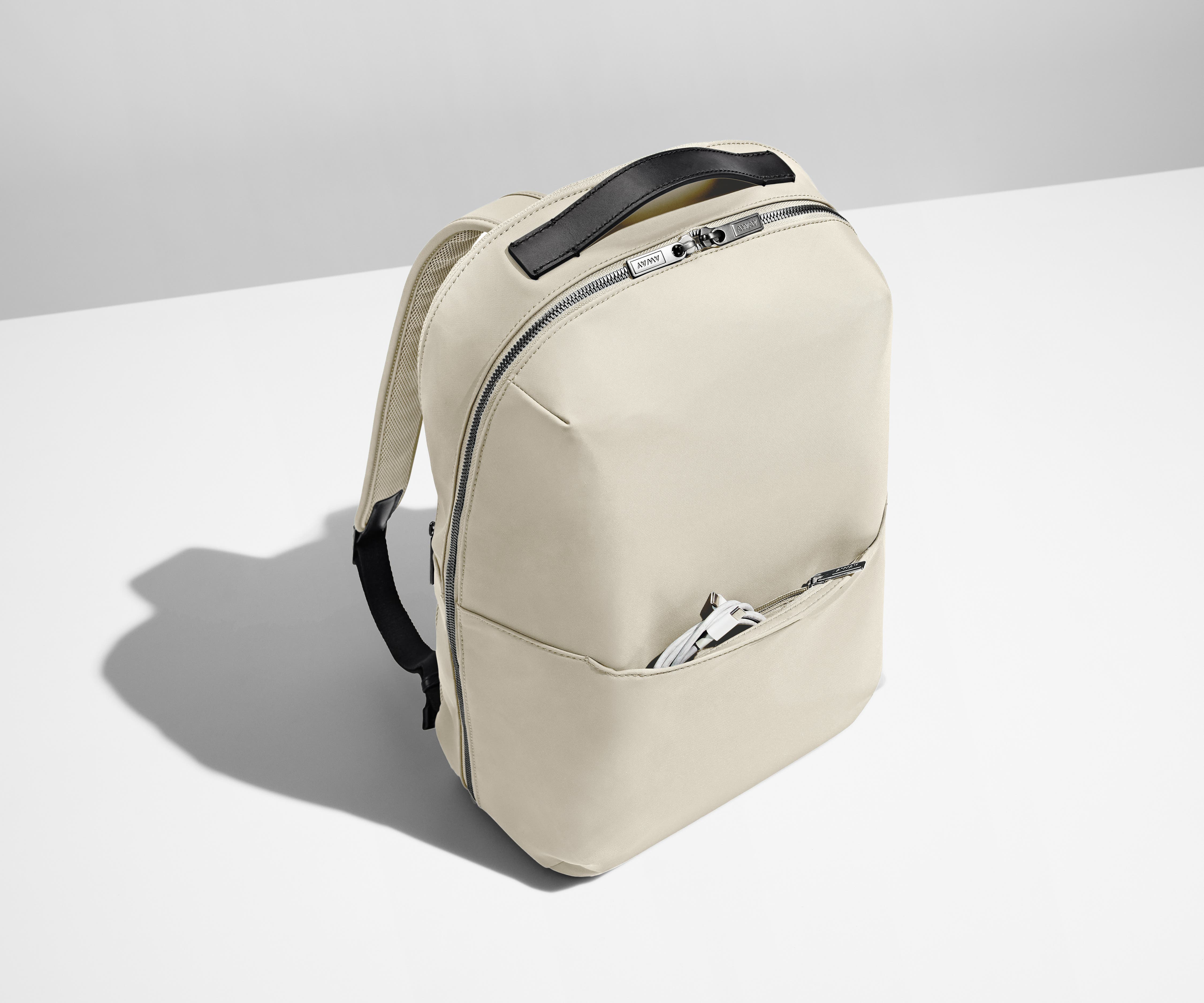 Angled product view of a Salt White Zip Backpack with a charging cord packed in the exterior front pocket