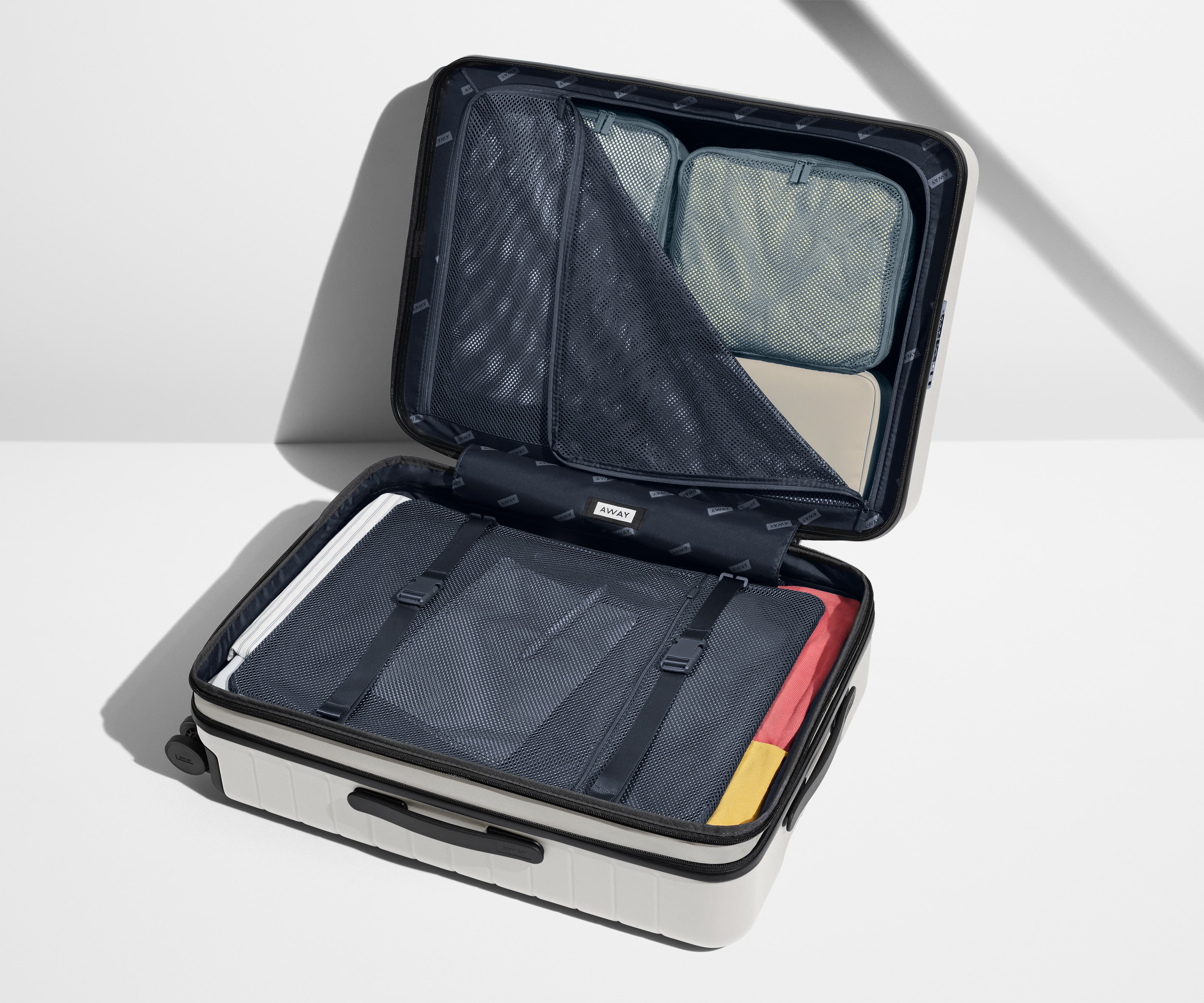 The Medium Flex suitcase in Cloud Gray shown open on its side and packed with Away's packing organizers to show capacity and the interior compression system, designed to help you pack more in
