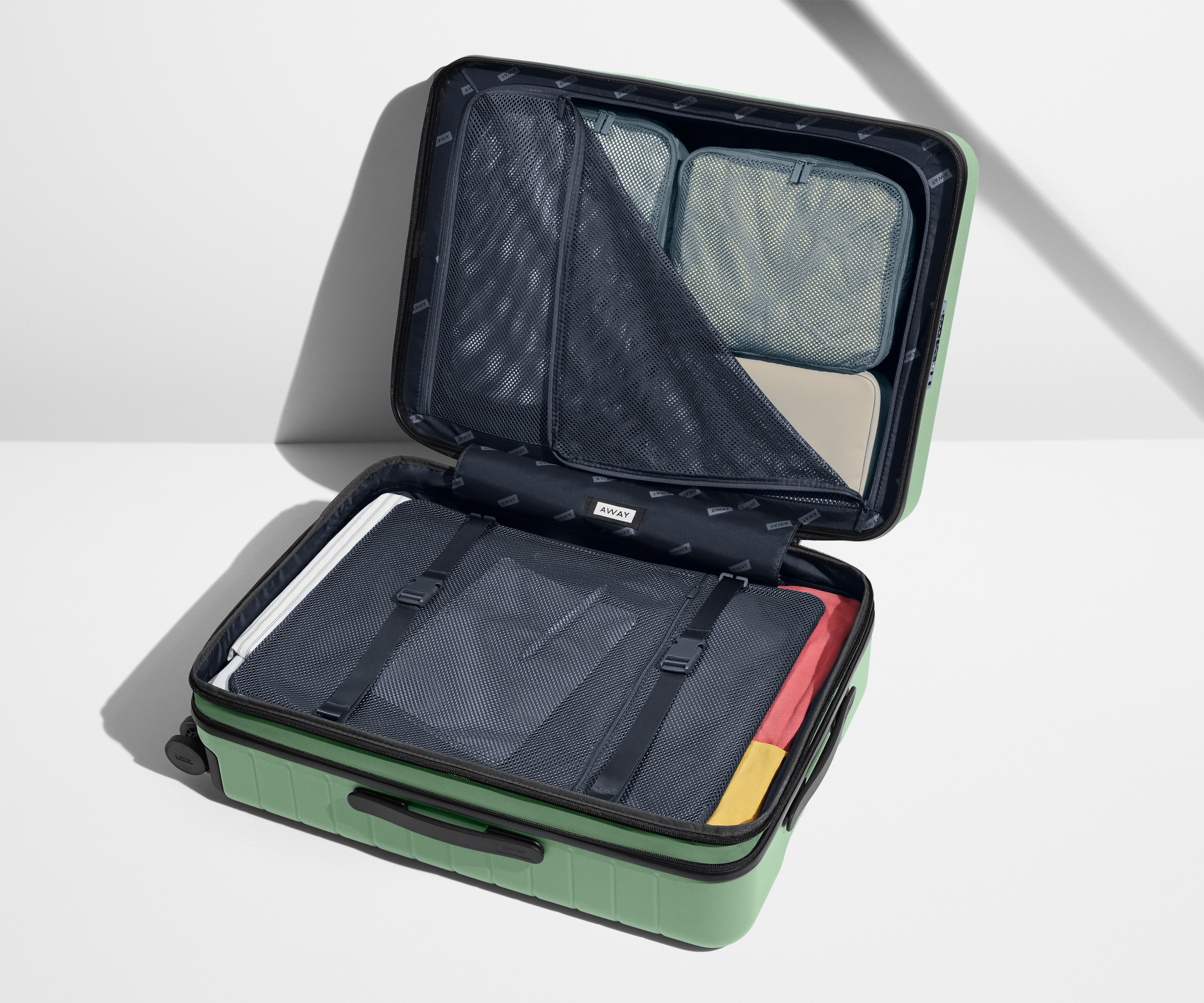 The Medium Flex suitcase in Sea Green shown open on its side and packed with Away's packing organizers to show capacity and the interior compression system, designed to help you pack more in