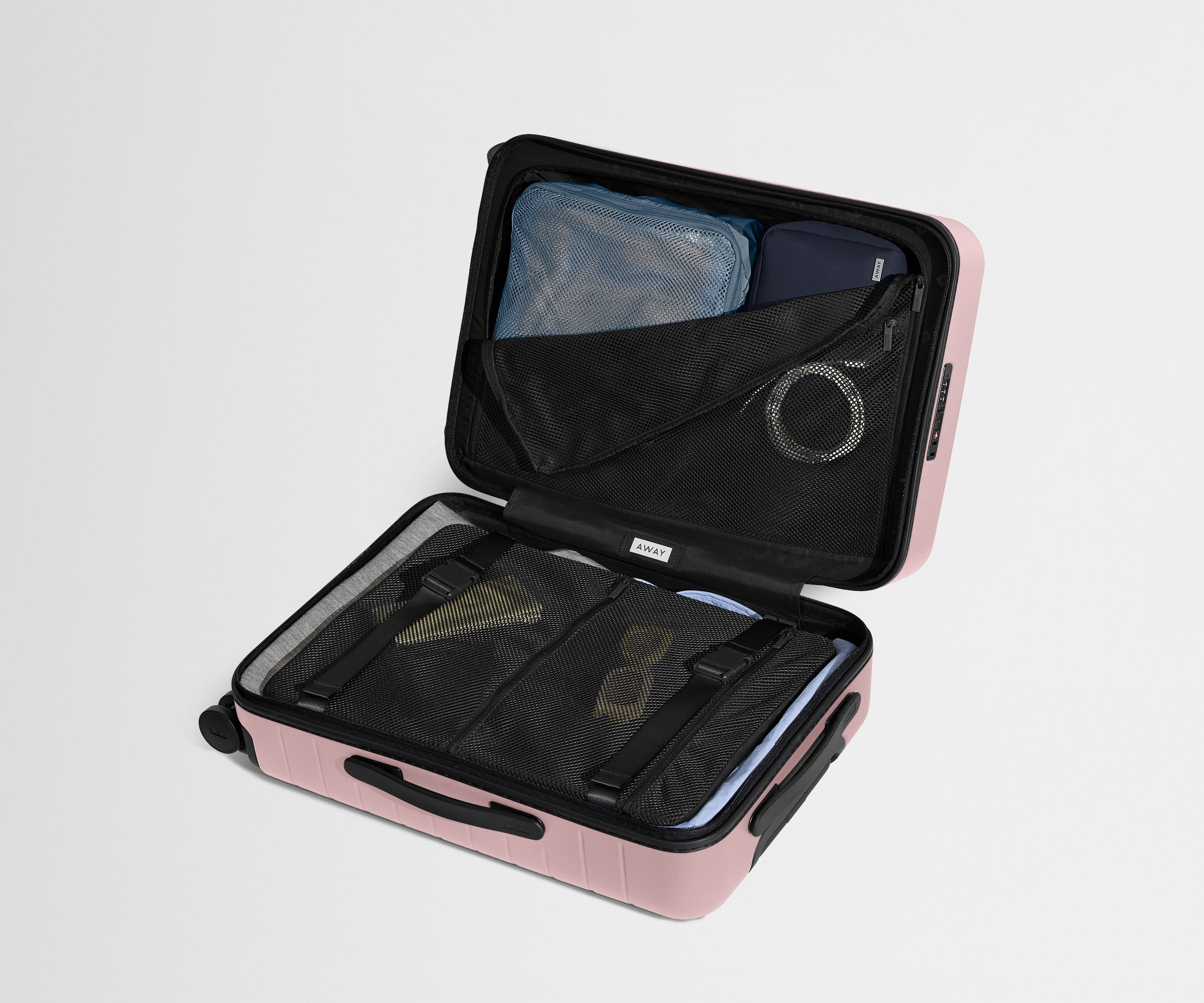 The Bigger Carry-On suitcase in Blush Pink shown open on its side and packed with Away's packing organizers to show capacity and the interior compression system, designed to help you pack more in