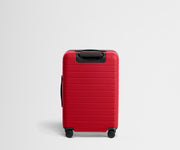 Red suitcase with black handle and wheels on a light gray background