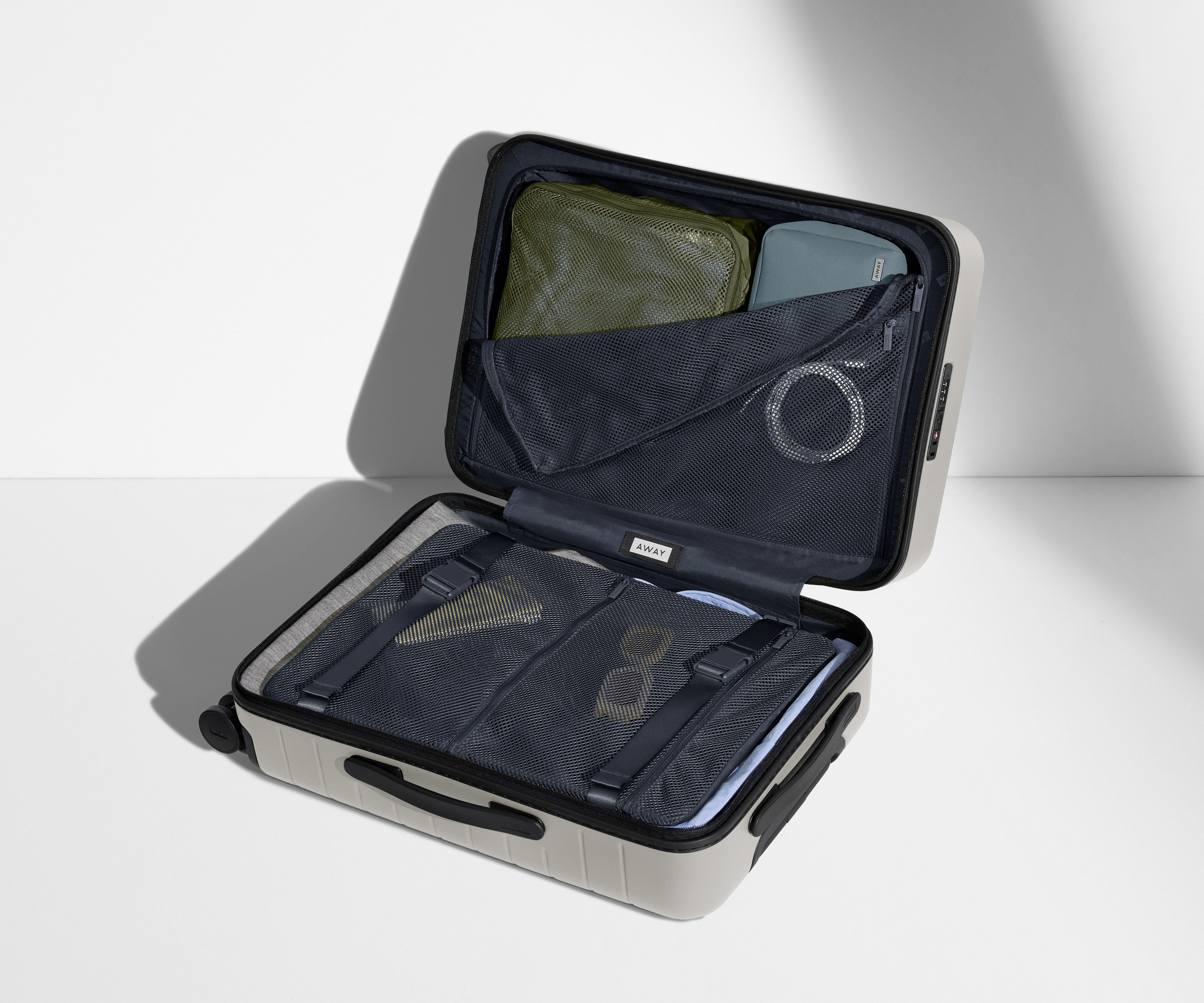 The Bigger Carry-On suitcase in Cloud Gray shown open on its side and packed with Away's packing organizers to show capacity and the interior compression system, designed to help you pack more in