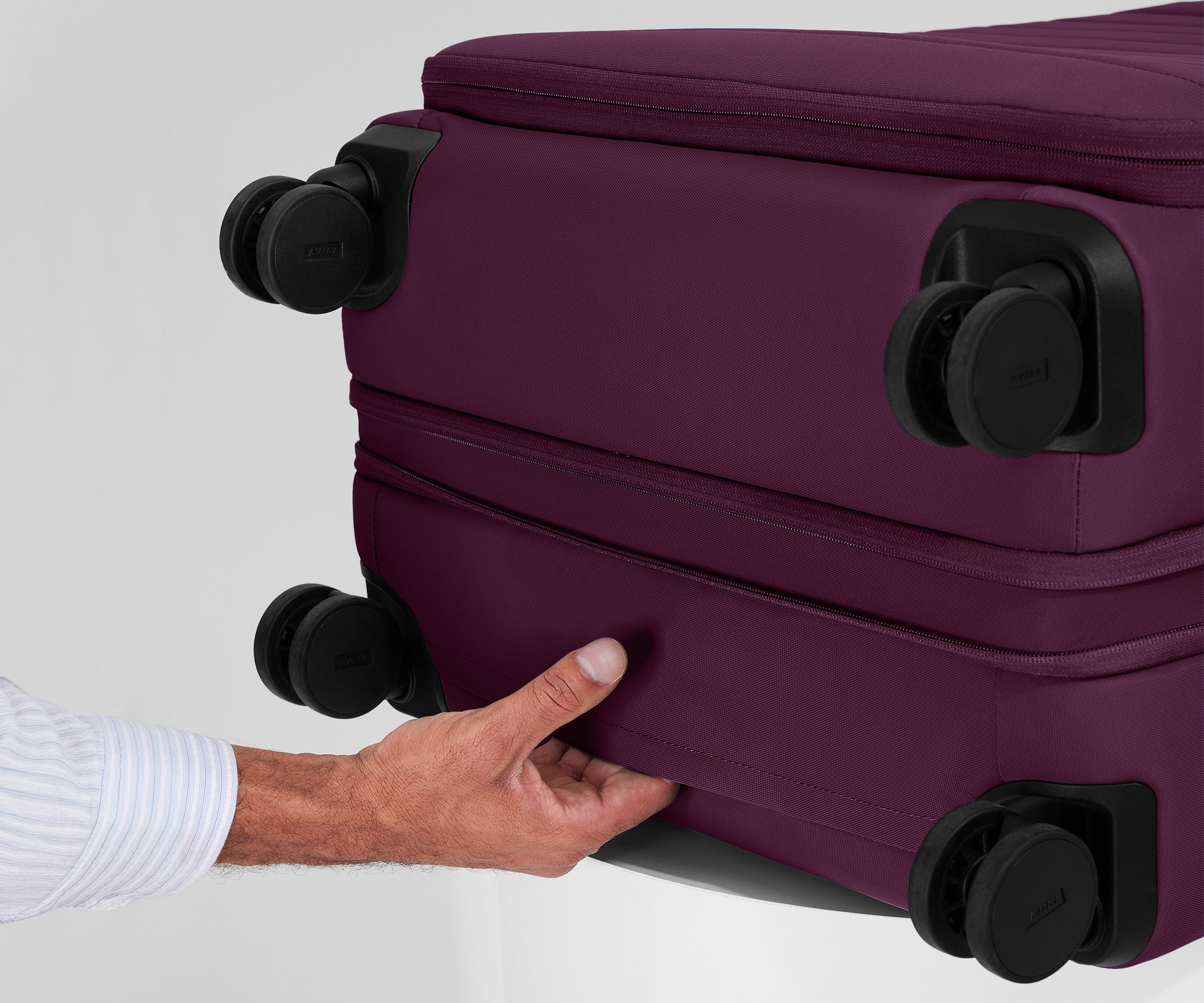 The Softside Large suitcase in Plum Purple shown laying on a surface to highlight the underside grab handle